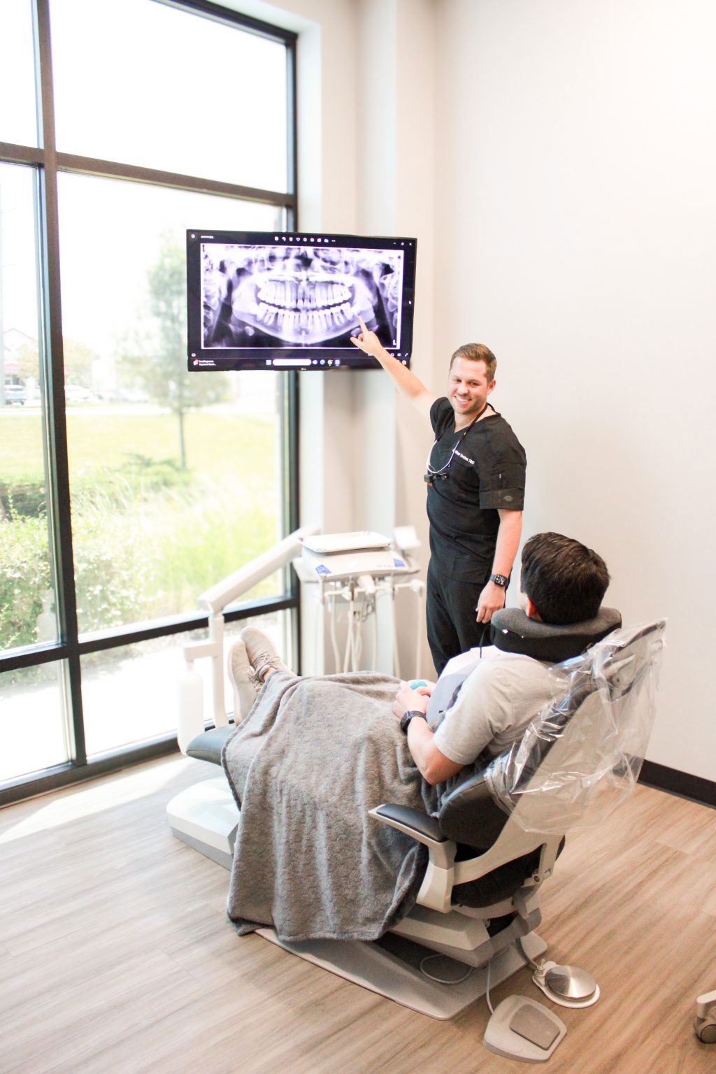 A man stands behind a dental chair with an open mouth model, pointing at it.