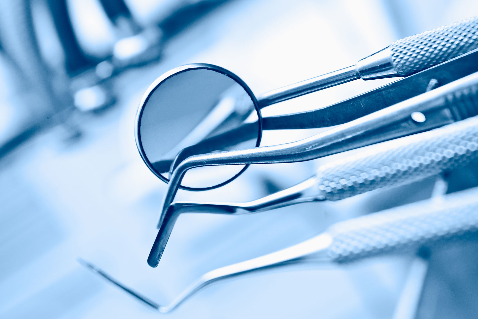 The image shows a collection of dental instruments, including tweezers and scissors, with a magnifying glass placed on top, all set against a blue background that resembles a medical setting.