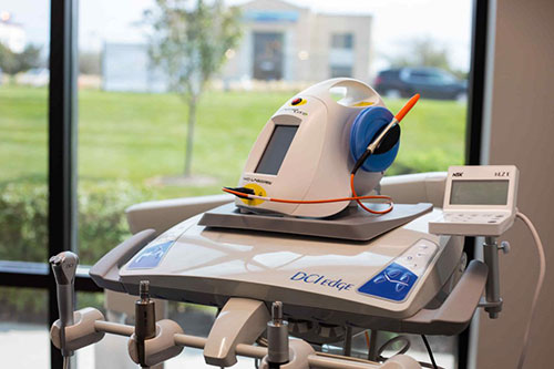 The image shows a medical device with a monitor displaying data, placed on top of a table, inside a room with a window.