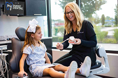 A dental hygienist interacting with a young girl in a dental office setting.