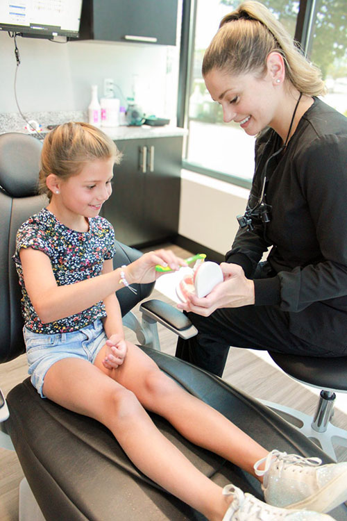 A young girl sitting on a dental chair, receiving dental care from an adult female dentist.