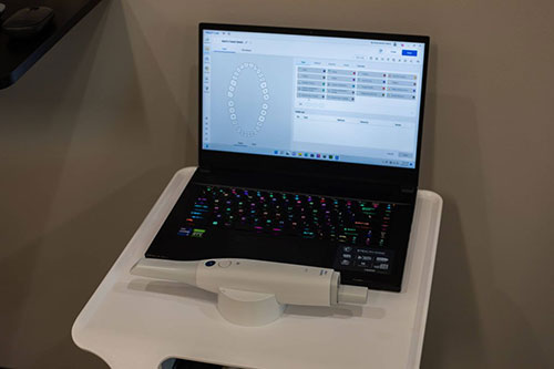 The image shows a laptop on a white desk with a medical device attached to its side, indicating some sort of medical or health-related activity.