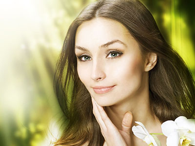 The image shows a woman with light skin and long hair, wearing makeup and looking directly at the camera. She has a serene expression and appears to be indoors with natural light illuminating her face.