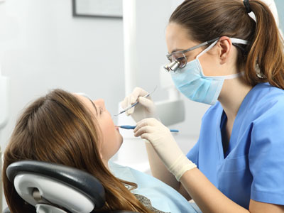 A dental hygienist performing a teeth cleaning procedure on a patient, with both individuals wearing medical masks and using specialized equipment.