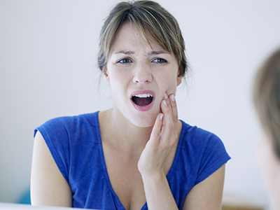 A woman with her mouth open, expressing surprise or shock, while looking at her reflection in a mirror.