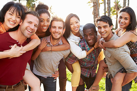 A group of young adults posing together outdoors, smiling and embracing each other.