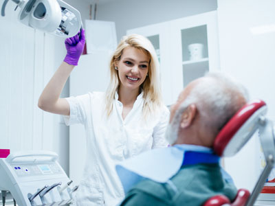 The image depicts a dental professional assisting an elderly patient with a dental chair setup.