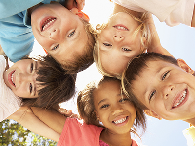 The image shows a group of children of various ages smiling at the camera while posing for a photo outdoors.