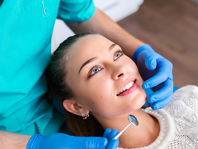 The image shows a dental hygienist performing a teeth cleaning procedure on a patient, with the dentist using specialized tools and the patient wearing protective eyewear.