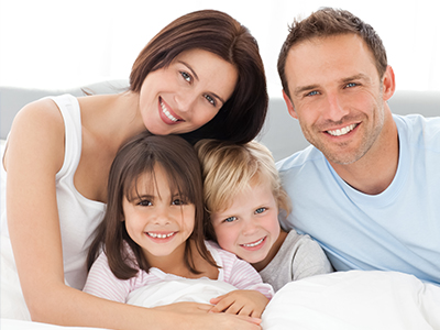 Family of four posing on bed with smiling faces.